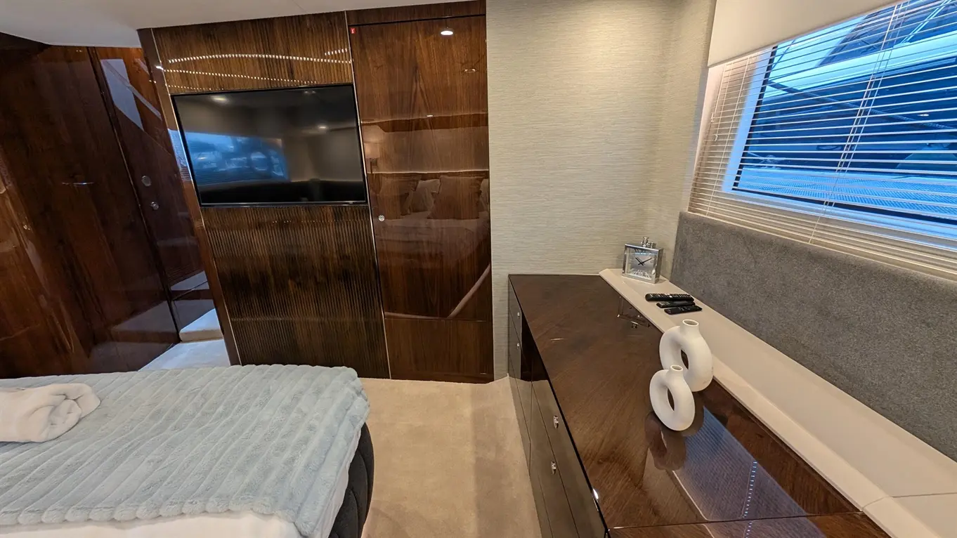 Luxurious yacht interior featuring a plush bed, sleek wooden cabinets, a TV, and decorative vases near a window.